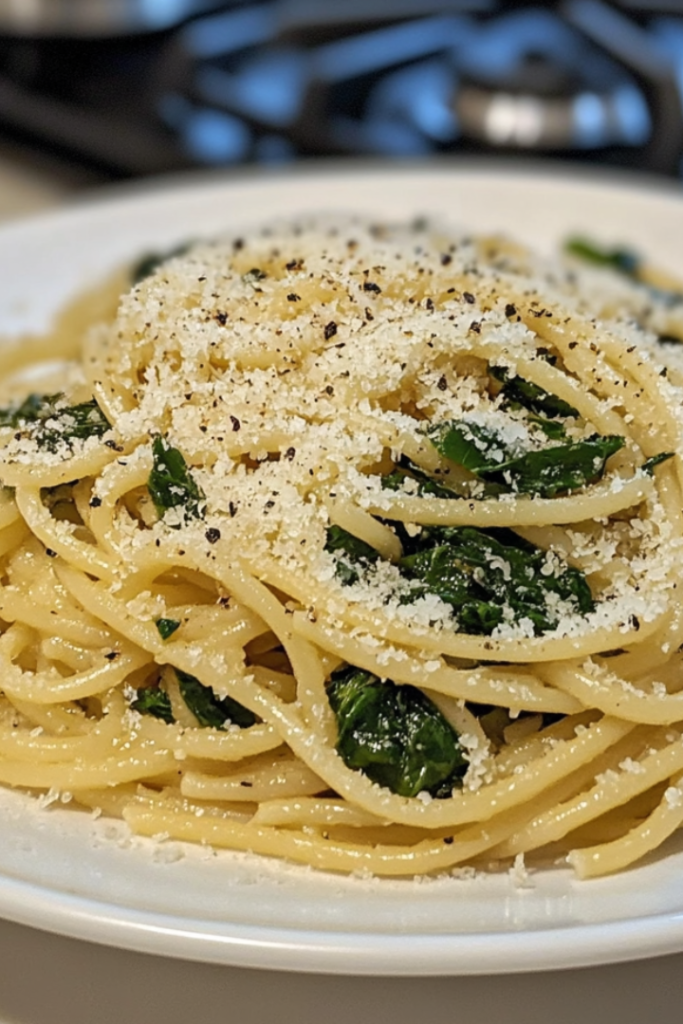 Close-up shot of the skillet on the white marble cooktop, with a sprinkle of vegan parmesan cheese on top of the pasta and spinach mixture, ready to serve