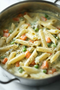 Close-up shot of al dente pasta being added to the thickened creamy vegetable mixture. The pasta is gently stirred into the sauce, absorbing the flavors as it simmers on the white marble cooktop