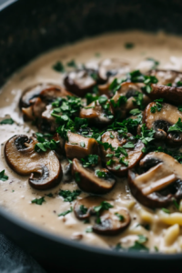 Close-up shot of cooked pasta being tossed in the creamy mushroom sauce in the skillet, with a sprinkle of fresh parsley on top, ready to serve
