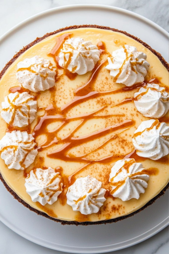 A creamy cheesecake on a plate, drizzled with salted butterscotch sauce and topped with whipped cream. A fork is beside the plate, ready to dig in.