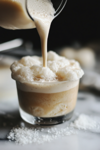 Sugar cookie cold foam being poured over a glass of iced coffee or cold brew, creating a frothy, festive layer on top.