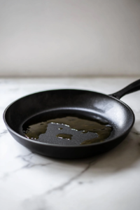 A large black skillet on a white marble cooktop with shimmering avocado oil heating over medium-high heat, ready for cooking