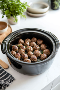 A slow cooker filled with frozen homestyle meatballs, evenly spread and ready for the addition of sauces. The slow cooker sits on a clean kitchen counter with a wooden spoon nearby