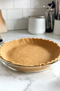A 9-inch unbaked vegan pie crust placed in a pie dish, ready for the filling. The crust edges are neatly crimped, and the oven is preheating to 350°F (180°C).