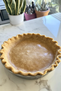 A 9-inch unbaked vegan pie crust resting in a pie pan, ready to be filled. The edges are crimped neatly, and the crust is chilling in the refrigerator.
