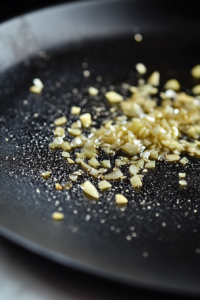 Close-up shot of diced yellow onion and minced garlic sizzling in the pan on the white marble cooktop, releasing their fragrance. The mixture is softening in the hot oil and butter