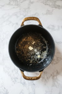 A Dutch oven on medium-low heat with butter melting as diced onions and minced garlic sizzle gently, releasing their fragrance. A pinch of salt and pepper is added for seasoning