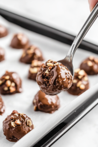 Close-up shot of the finished chocolate-nut clusters, firming up on parchment paper after about an hour. The candies are now set and ready to be transferred to an air-tight container, with the white marble cooktop in the background.