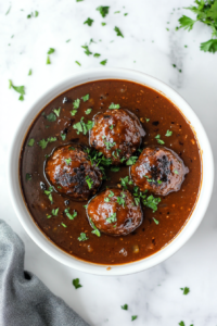 Cooked meatballs served straight from the slow cooker, with the glossy BBQ and grape jelly sauce glistening on the meatballs. Optional garnishes like chopped parsley are sprinkled on top for presentation