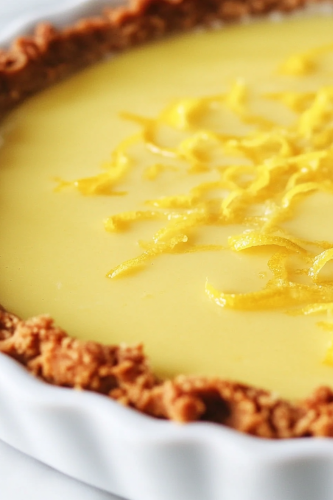 Close-up shot of the lemon pie filling being poured into the prepared cookie crust. The filling smoothly settles into the base, ready to be refrigerated and set. The pie dish is placed in the fridge to firm up.