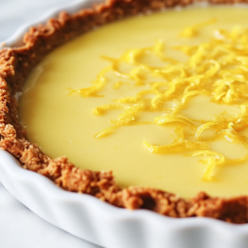 Close-up shot of the lemon pie filling being poured into the prepared cookie crust. The filling smoothly settles into the base, ready to be refrigerated and set. The pie dish is placed in the fridge to firm up.