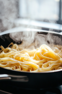 Fresh fettuccine pasta boiling in water, with steam rising as the noodles cook to perfection, ready to be combined with the sauce.