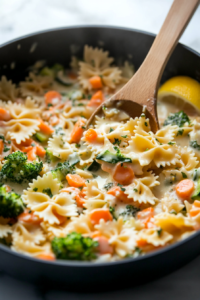 A beautifully plated bowl of creamy coconut milk pasta with mixed vegetables like carrots, zucchini, and cherry tomatoes. A sprinkle of vegan parmesan and fresh parsley completes the dish.