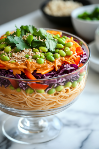 Using tongs to toss the ingredients in a large bowl, mixing the pasta and vegetables with the creamy peanut sauce. The dish is garnished with sesame seeds and ready to serve.