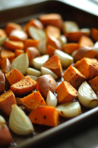 A baking sheet filled with diced sweet potatoes, halved garlic cloves, and halved shallots tossed in olive oil, ready to roast in a preheated oven at 450°F. The vegetables are golden brown and caramelized after 25 minutes.