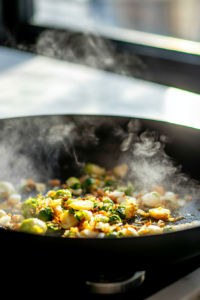 A close-up of a pan with halved Brussels sprouts and finely chopped garlic sizzling in olive oil. The edges of the sprouts are golden brown, and steam rises from the pan.