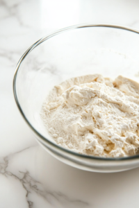 Close-up shot of the mixing bowl, with flour, vanilla extract, sour cream, and heavy whipping cream added to the cheesecake batter, being mixed gently.