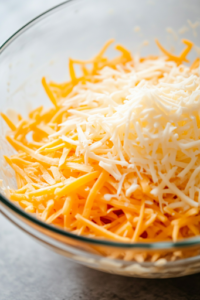 A close-up view of condensed cream of chicken soup, sour cream, and shredded cheddar cheese being added to the bowl of hashbrowns. The creamy ingredients begin to blend, creating a rich, flavorful mixture. The scene is set on a white marble cooktop.