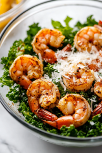 The fully assembled Kale Cajun Shrimp Salad in a glass salad bowl on a white marble cooktop. Freshly grated Parmesan cheese is sprinkled on top, completing the dish, with a fork resting nearby, ready to dig in.
