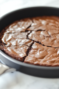 The baked Vegan Chocolate Pudding Cake in the pan on a white marble cooktop. The top is slightly cracked, with gooey chocolate sauce bubbling beneath the surface.