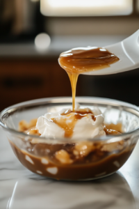 A close-up shot of a glass mixing bowl on a white marble countertop, where cream cheese, brown sugar, and flour are being beaten with a hand mixer until smooth.