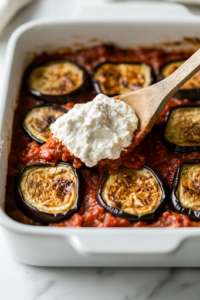A black skillet filled with browned beef, simmering with rich keto tomato sauce and dried basil. A wooden spoon stirs the fragrant mixture, releasing a deep, savory aroma over the white marble cooktop.