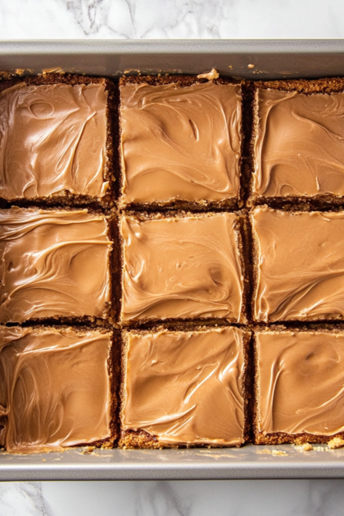 Warm caramel frosting being poured over cooled cookie bars, with a spatula spreading it evenly