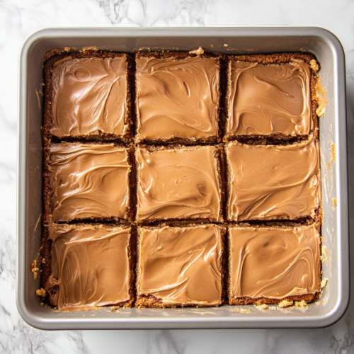Warm caramel frosting being poured over cooled cookie bars, with a spatula spreading it evenly