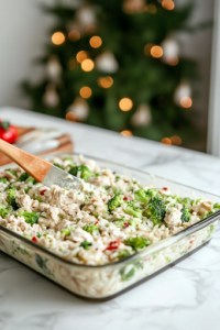 A greased 9×13-inch glass baking dish sits on the white marble cooktop, with the creamy chicken, rice, and broccoli mixture being spread evenly using a spatula. The surface is smooth and level, ready for baking.