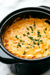 A black crockpot on a white marble cooktop, as the Buffalo chicken dip cooks on low heat. The cheese starts to melt, and the mixture gradually turns smooth and creamy, filling the kitchen with a rich, tangy aroma.