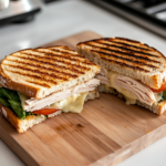 A fully grilled Turkey and Pepper Jack sandwich, sliced in half on a wooden cutting board over the white marble cooktop. The melted cheese stretches between the layers, while the crispy golden bread glistens from the buttery grilling.