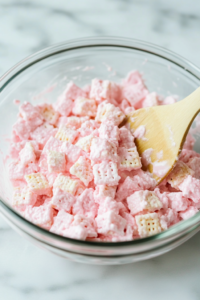 A zip-top bag filled with pink-coated Chex cereal and powdered sugar, being shaken to coat evenly.