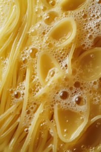Close-up shot of a pot of salted water boiling, with broken-in-half spaghetti cooking inside. The pasta is nearly al dente and ready to be drained.
