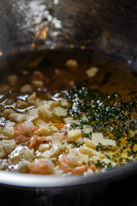 A large pot with melted butter sizzling, as medium shrimp cook and turn pink. Minced garlic is added to the pot, creating a fragrant aroma.