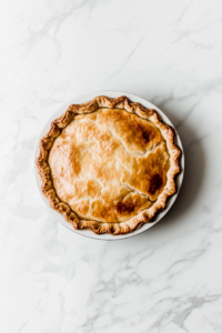 A freshly baked vegan treacle tart cooling on the white marble cooktop. A slice is gently cut out, showing the golden crust and slightly oozing apple filling.