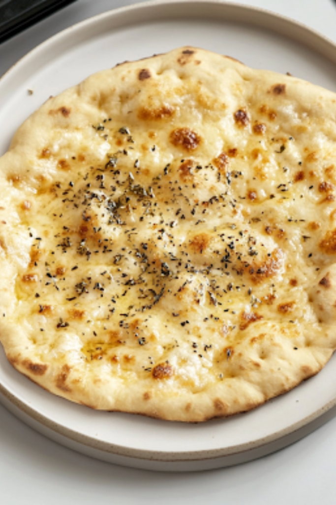 A warm, golden flatbread resting on a plate over the white marble cooktop, lightly sprinkled with oregano, ready to be enjoyed as a savory and satisfying dish.
