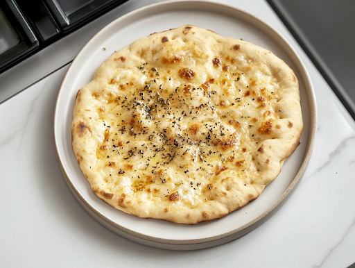 A warm, golden flatbread resting on a plate over the white marble cooktop, lightly sprinkled with oregano, ready to be enjoyed as a savory and satisfying dish.