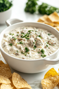 A close-up shot of a serving bowl filled with warm, creamy queso dip, placed on a white marble countertop. The queso is surrounded by crispy tortilla chips and fresh veggie dippers, making it the perfect appetizer, ready to be enjoyed.