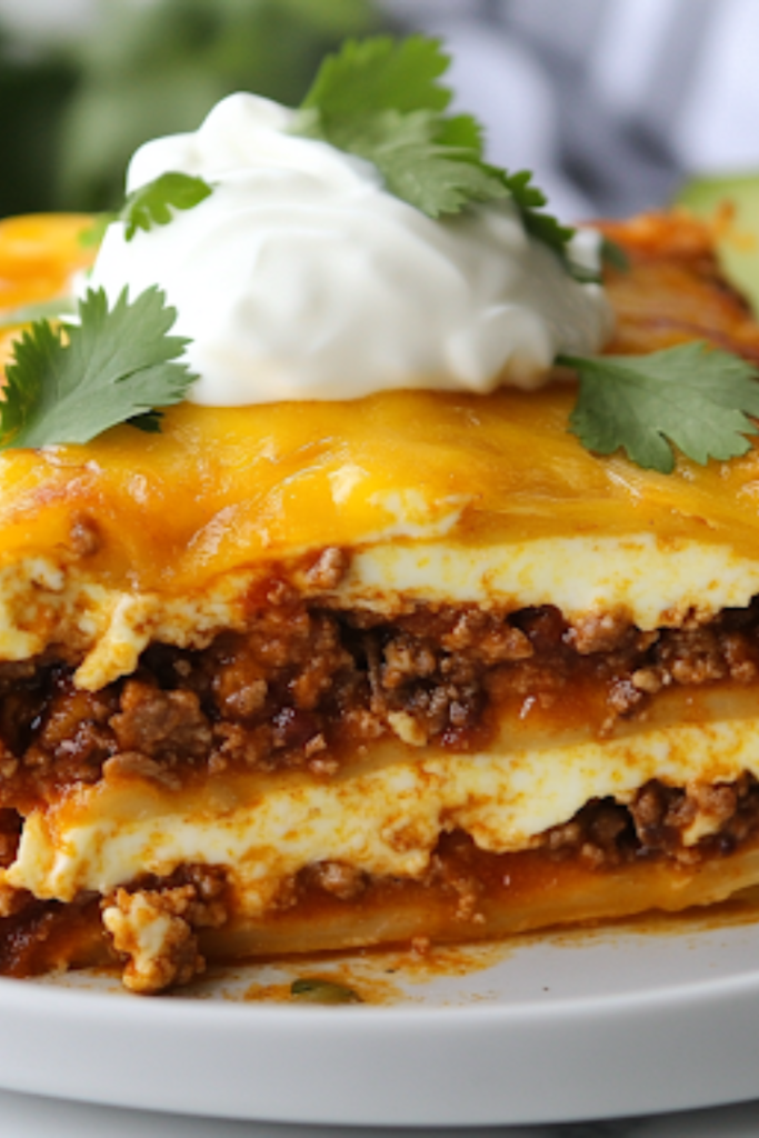 A close-up of a sliced portion of taco casserole on a plate, garnished with fresh cilantro, sour cream, and a slice of avocado. The layers of seasoned beef, creamy eggs, and melted cheese are visible, making each bite look hearty and delicious.