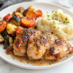 A close-up shot of a plate of garlic butter chicken served hot with a side of roasted vegetables and mashed potatoes on a white marble countertop. Steam rises, highlighting the dish’s fresh, savory appeal, ready to be enjoyed.
