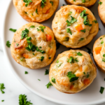 A serving plate with warm, golden-brown chicken pot pie muffins, garnished with fresh parsley. The plate sits on the white marble cooktop, ready to be enjoyed as a comforting homemade meal.
