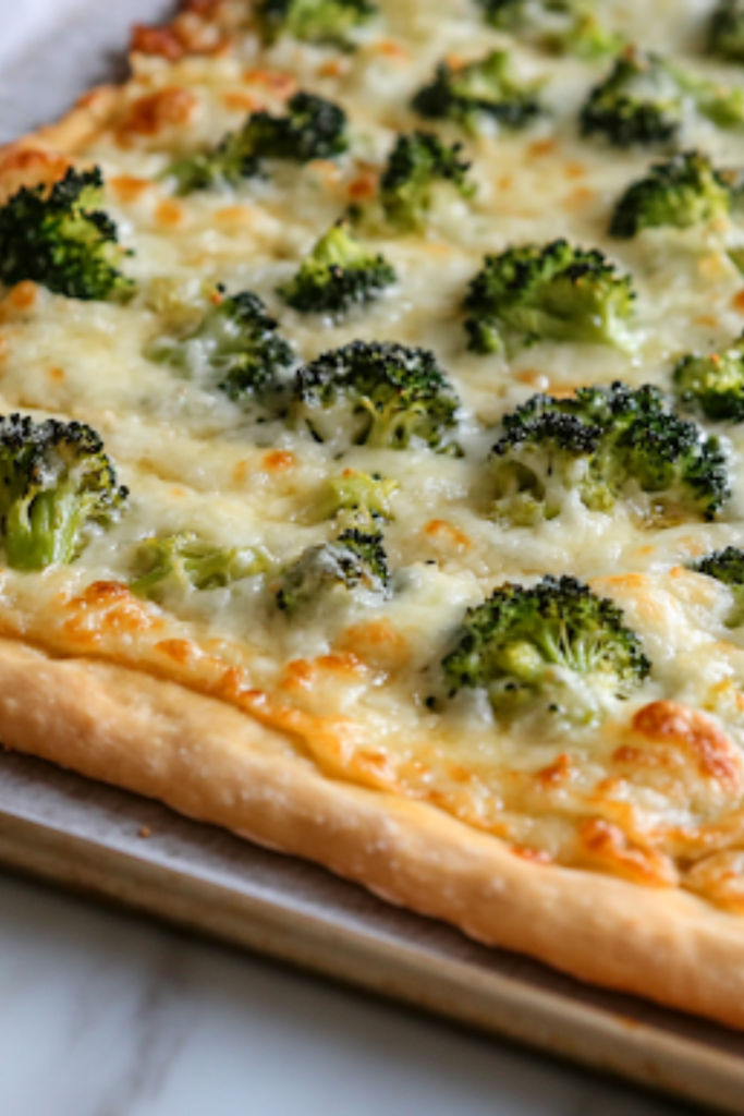 A close-up of the finished Keto Broccoli White Pizza on a parchment-lined baking sheet. The melted cheese is bubbly, the edges are crisp, and the broccoli is slightly roasted, ready to be sliced and enjoyed.