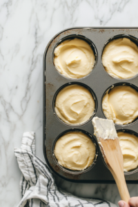 A spoon carefully pouring the pink-tinted cream cheese filling into the pre-baked graham cracker crusts in a mini cheesecake pan.