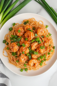 A plated serving of Bang Bang Shrimp Pasta on a white dish, garnished with bright green chopped scallions. A fork is twirling some noodles, ready to be enjoyed.