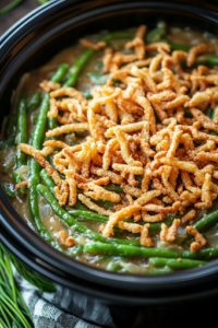 A close-up shot of the finished green bean casserole in the slow cooker, with a crispy layer of golden-brown French-fried onions on top. The casserole is perfectly baked, with a rich aroma filling the kitchen.