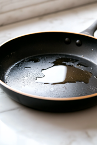 A deep black skillet on a white marble cooktop, filled with hot vegetable oil shimmering at 350°F. A thermometer is clipped to the side, ensuring the perfect frying temperature for crispy chicken.