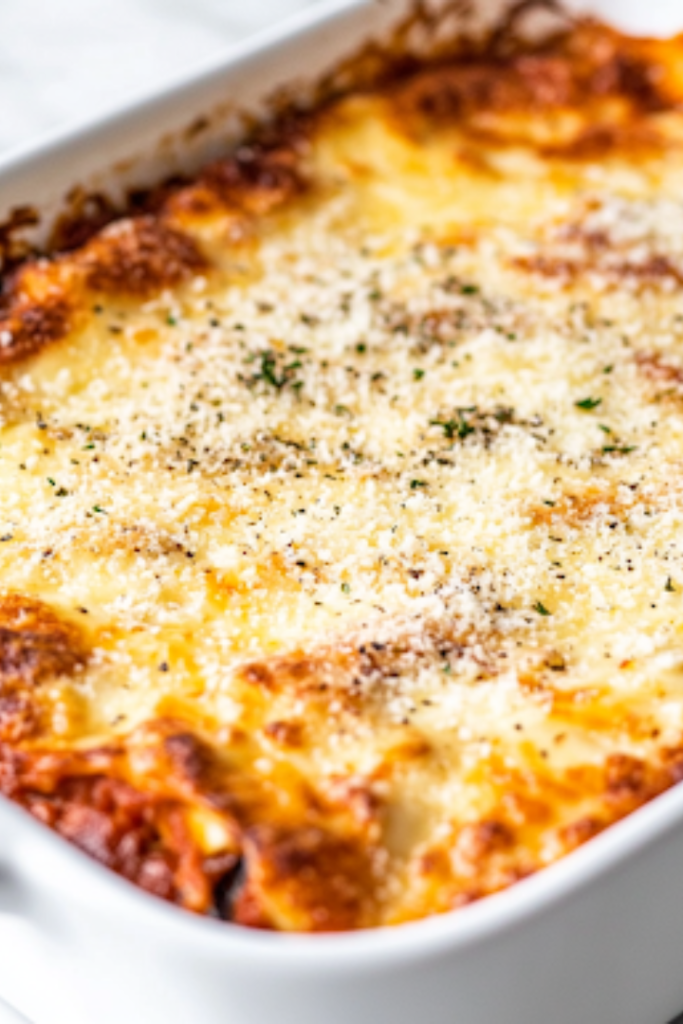 A freshly baked keto eggplant lasagna in a white ceramic baking dish on a white marble cooktop. The top is covered with bubbling, golden-brown mozzarella and Parmesan cheese, resting for 10 minutes before slicing.