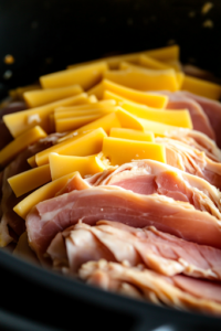 Thin slices of ham being carefully placed over each chicken breast in the slow cooker, followed by slightly overlapping slices of Swiss cheese. The layers add a rich, savory flavor to the dish.