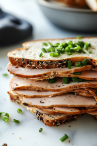 Half of the sourdough bread slices on a white marble cooktop, topped with thinly sliced deli turkey. Freshly chopped green onions are sprinkled on top, adding a pop of color and a hint of sharp, savory flavor.
