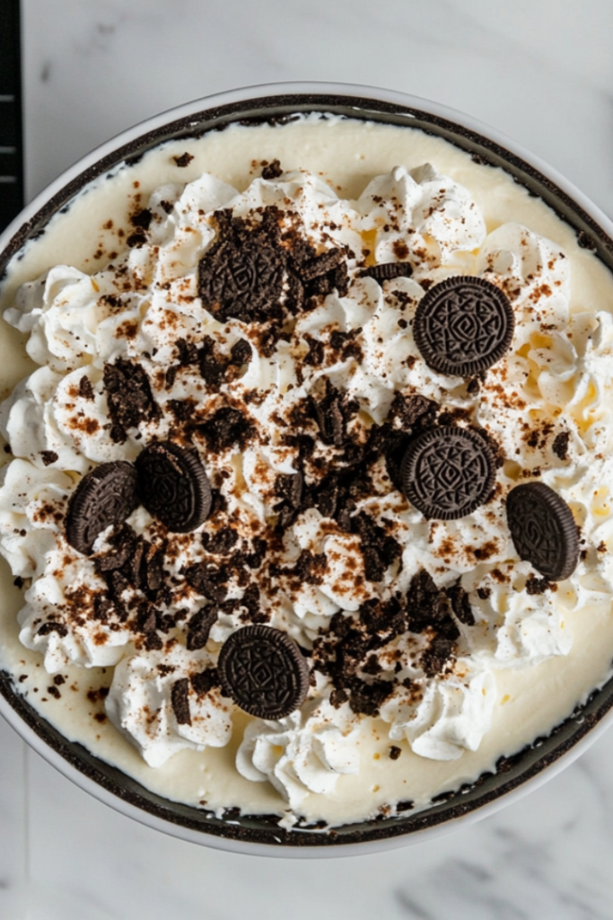 The chilled Oreo cheesecake topped with piped whipped cream, additional crushed Oreos, and a drizzle of hot fudge.